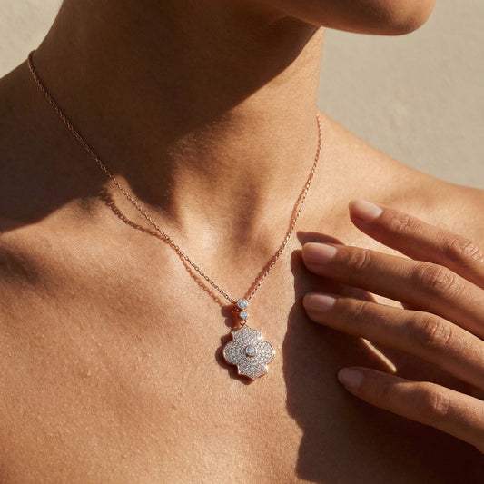 Necklace with a floral pendant worn by a person, with a hand touching the skin.
