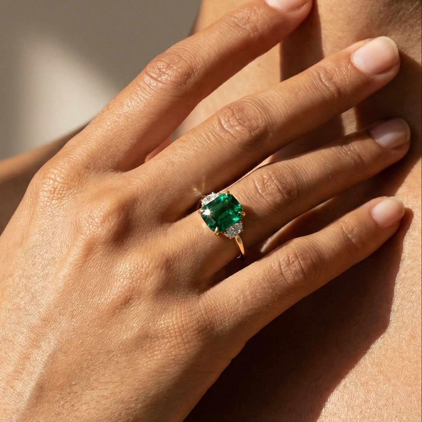 Hand wearing a green gemstone ring on a neutral background