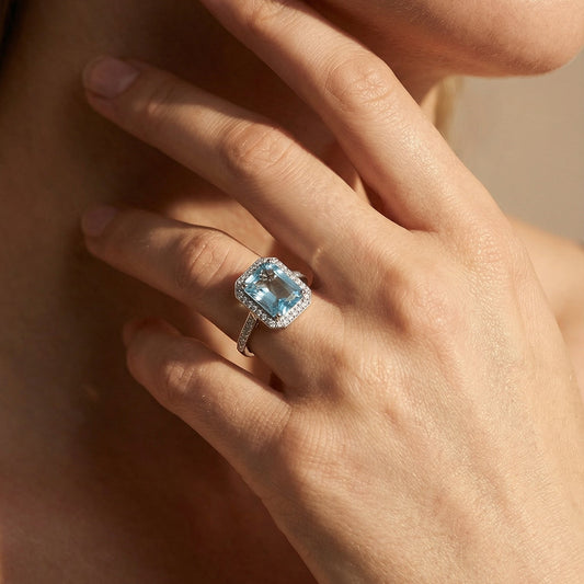 Close-up of a hand wearing a ring with a blue gemstone, touching the neck.