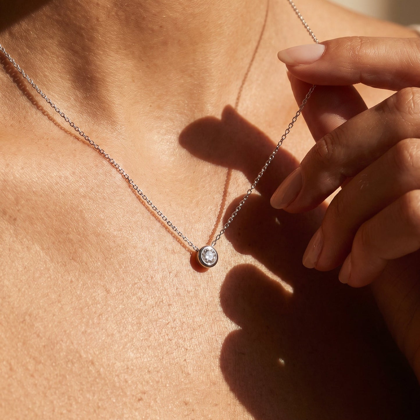 WHite gold Solo single diamond necklace made in Marlow Person wearing a delicate necklace with a small pendant, close-up on skin.