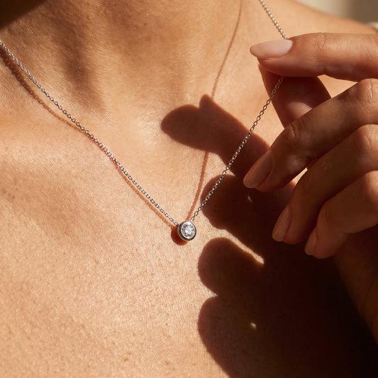 WHite gold Solo single diamond necklace made in Marlow Person wearing a delicate necklace with a small pendant, close-up on skin.
