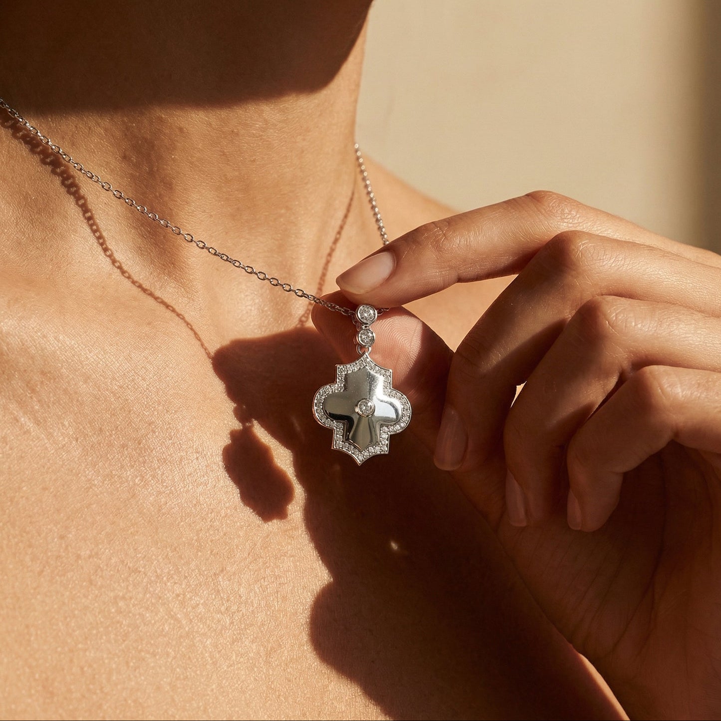 Person wearing a necklace with a decorative pendant, held by a hand against a neutral background