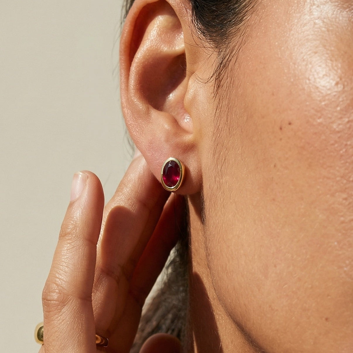 Close-up of a person wearing a red earring with a neutral background