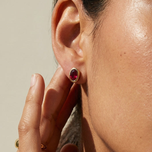 Close-up of a person wearing a red earring with a neutral background