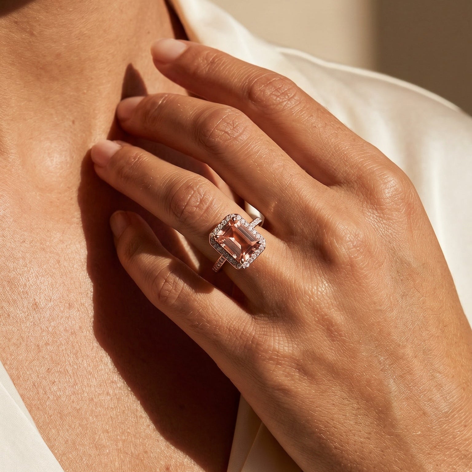 Close-up of a hand wearing pink tourmaline stone ring with a diamond, touching the neck against a neutral background.