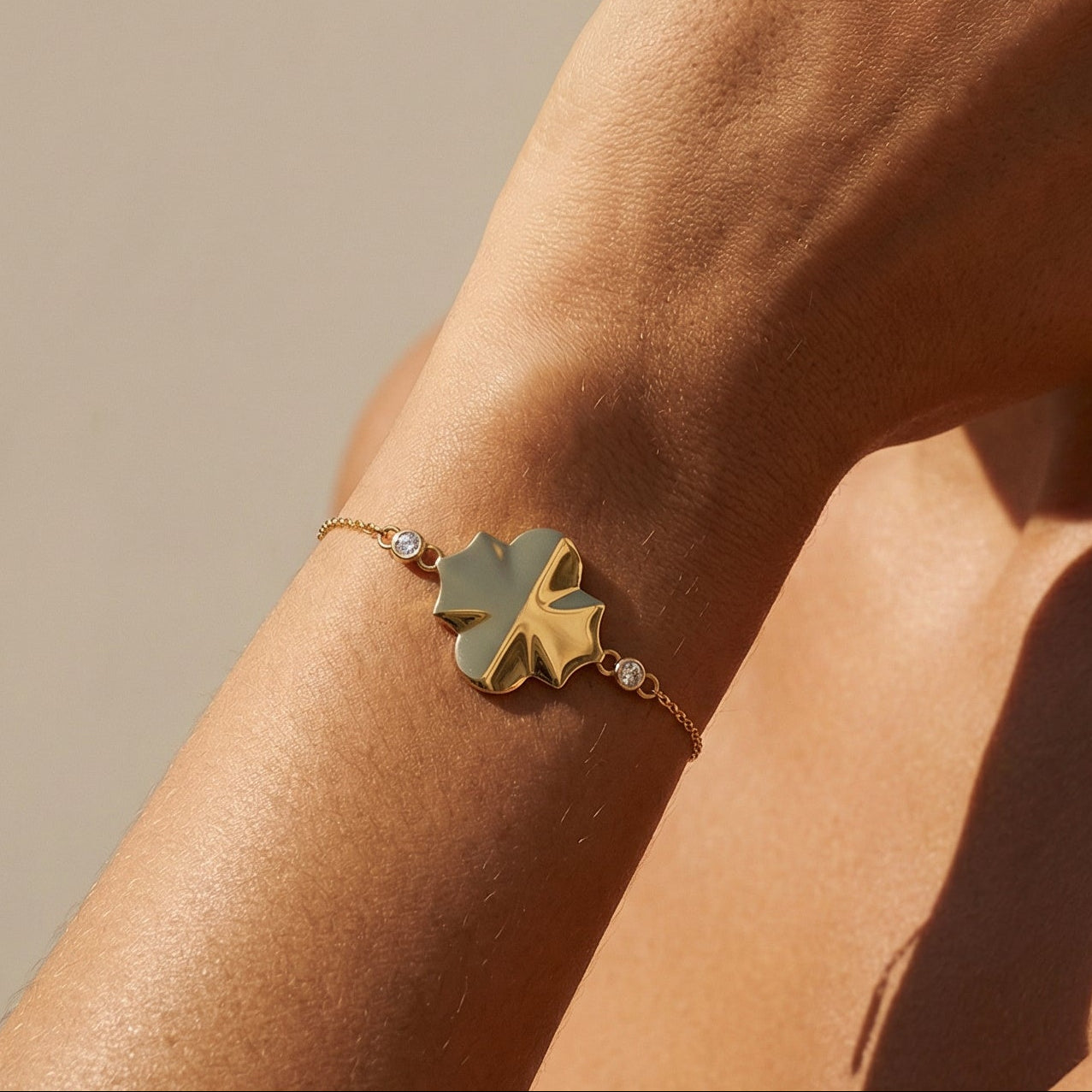 Close-up of a person wearing a gold bracelet with a leaf design on a neutral background
