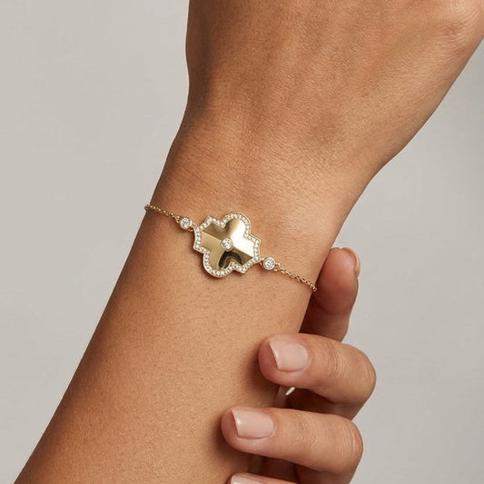 Hand wearing a gold bracelet with a geometrical diamond charm on a neutral background