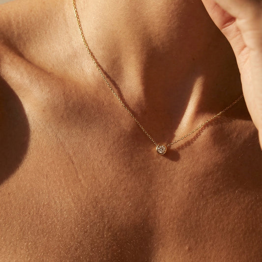 Close-up of a person wearing a delicate necklace with a small pendant on a neutral background