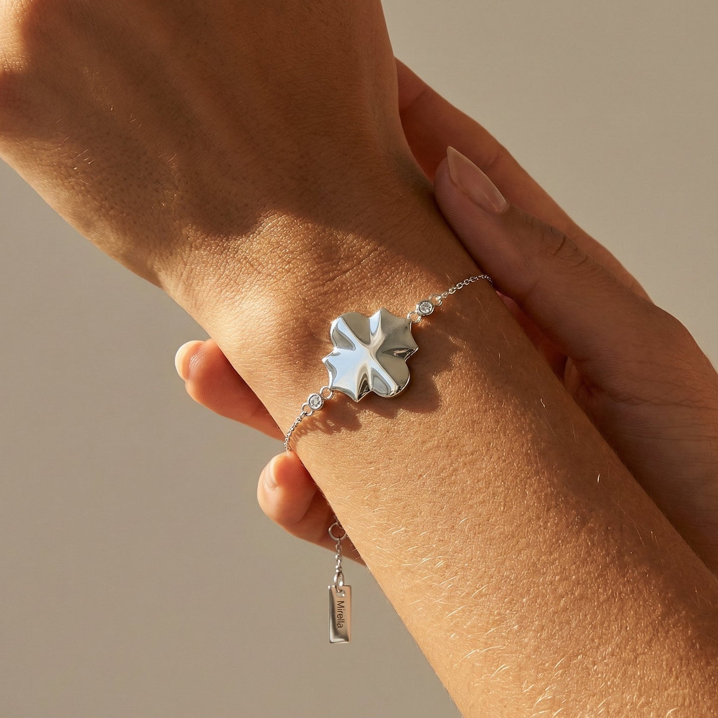 Silver bracelet with a clover-shaped charm on a wrist against a neutral background