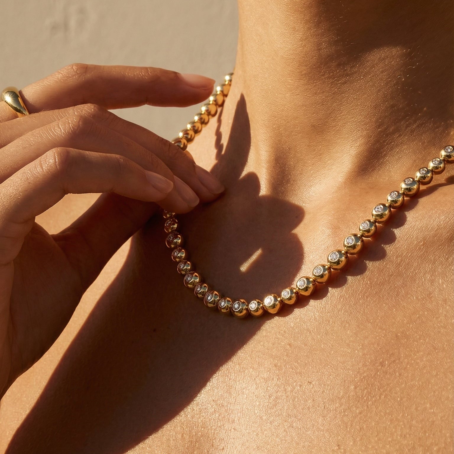 Close-up of a person wearing a gold necklace against a neutral background