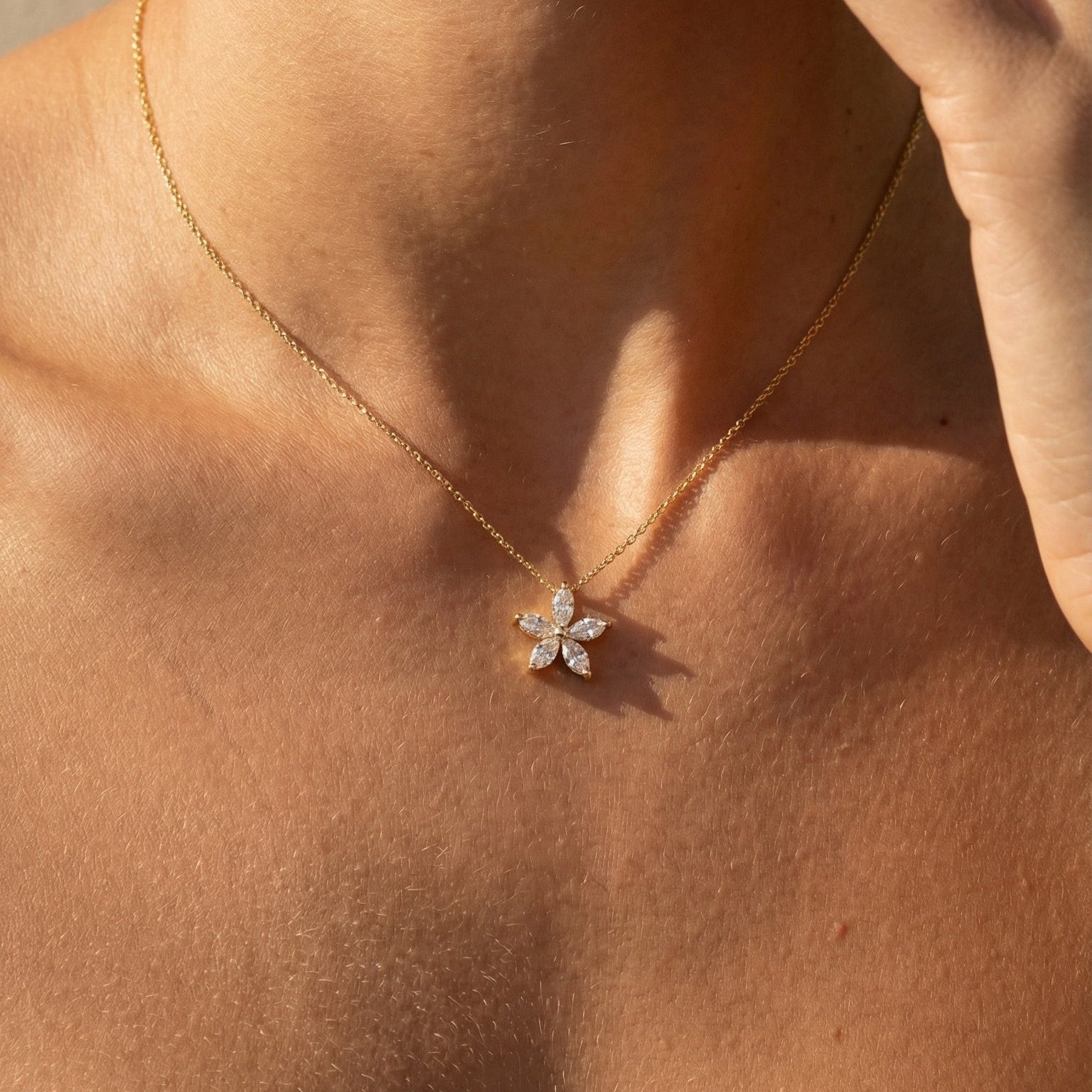 Close-up of a necklace with a flower pendant on a person's neck.