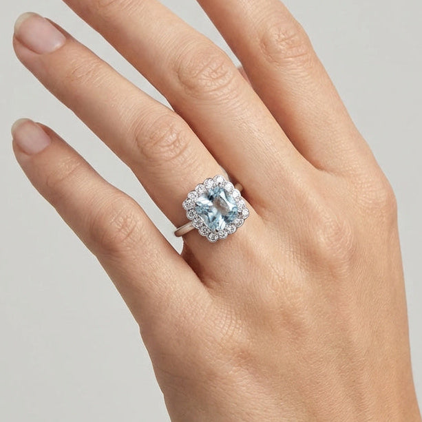 Hand wearing a diamond and aquamarine  ring on a neutral background