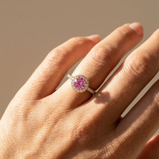 Hand wearing a ring with a pink gemstone on a neutral background
