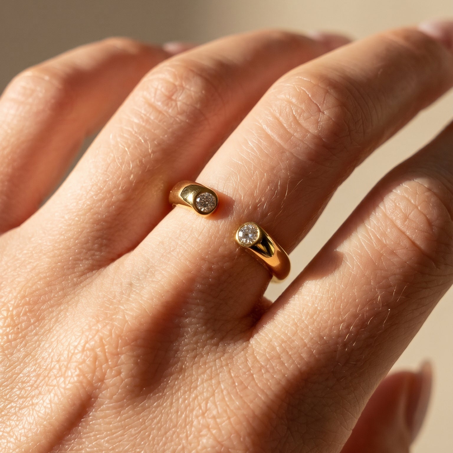 Close-up of a hand wearing two gold rings with gemstones on a neutral background