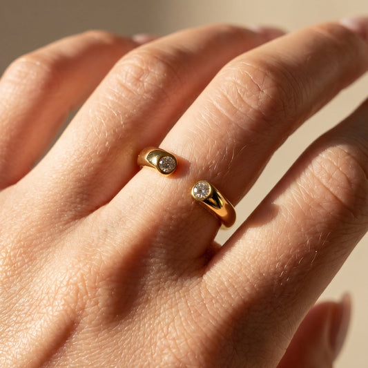 Close-up of a hand wearing two gold rings with gemstones on a neutral background