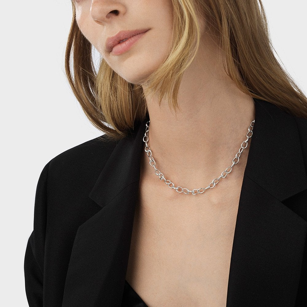 Person wearing a silver chain necklace with a plain background