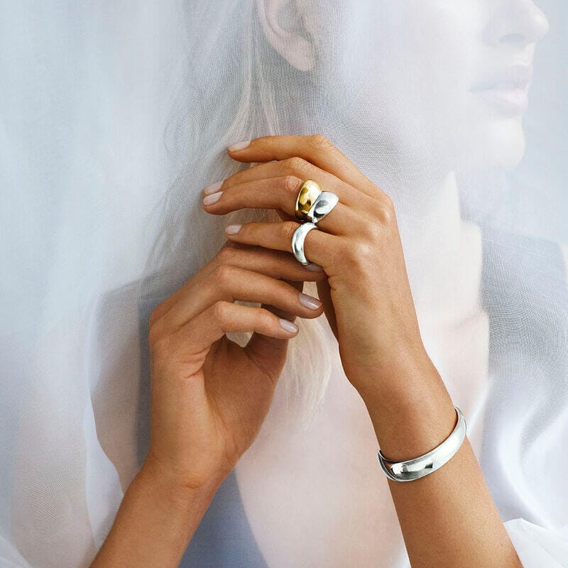 Close-up of hands wearing gold and silver rings with a light background