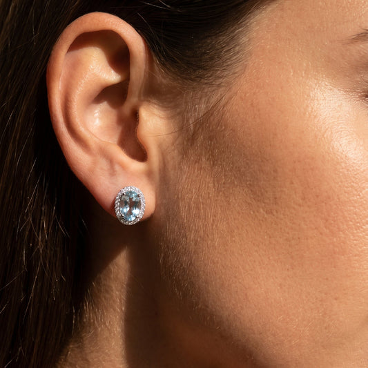 Close-up of a person wearing a silver earring with a blue gemstone.