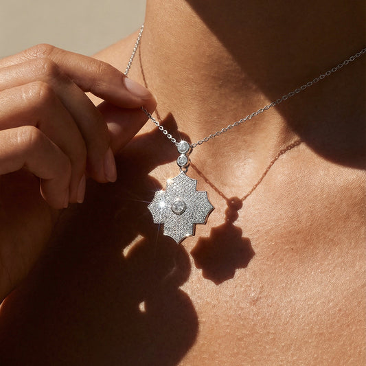 Close-up of a person wearing a silver necklace with a pendant on a neutral background