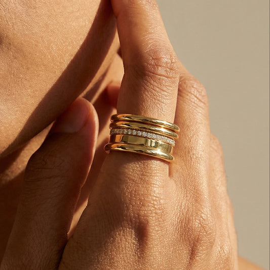 Close-up of a hand with a wide yellow gold ring with diamonds on a neutral background