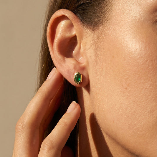 Close-up of a person wearing green emerald earrings with a neutral background