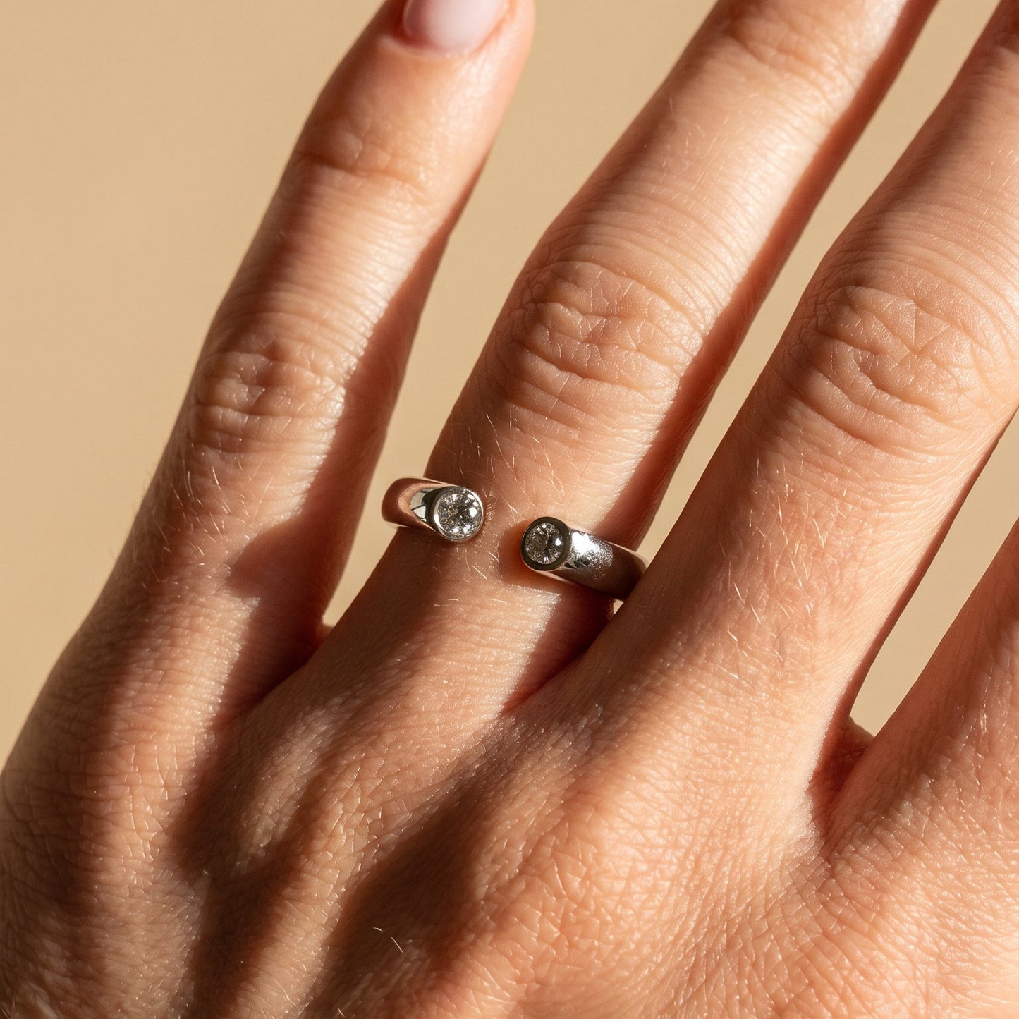 Hand wearing a silver ring with small stones on a beige background