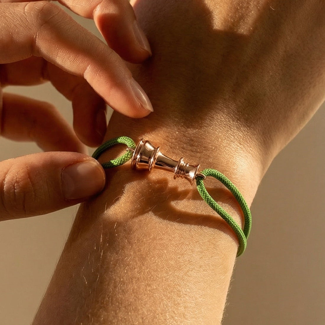 Person adjusting a green bracelet on their wrist against a neutral background