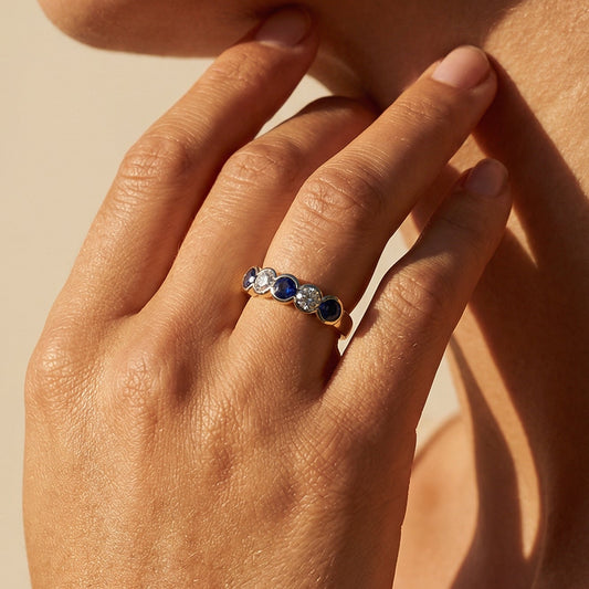 Close-up of a hand wearing a ring with a blue gemstone, touching the neck against a beige background