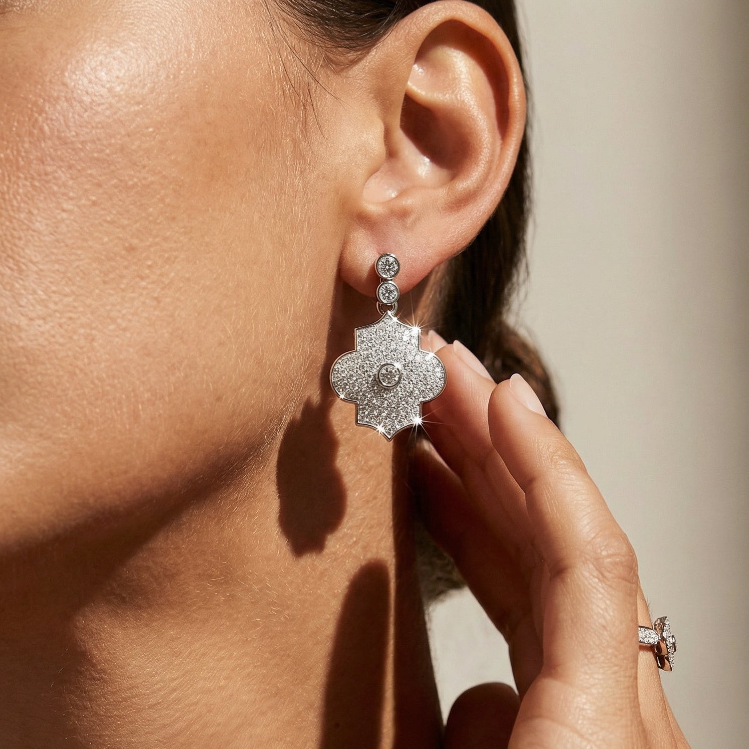 Close-up of a woman wearing sparkling silver earrings with a neutral background