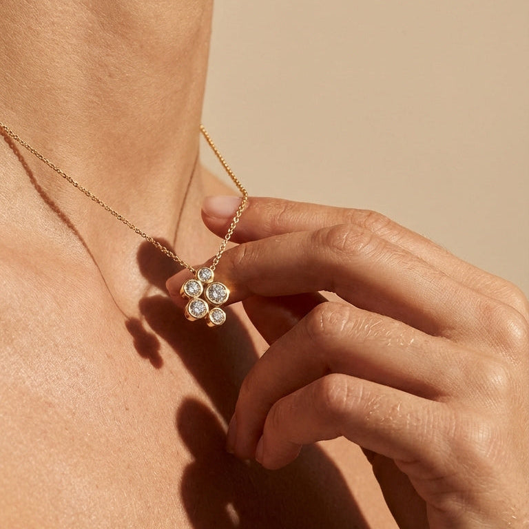 Close-up of a person wearing a delicate gold necklace with a small pendant on a beige background