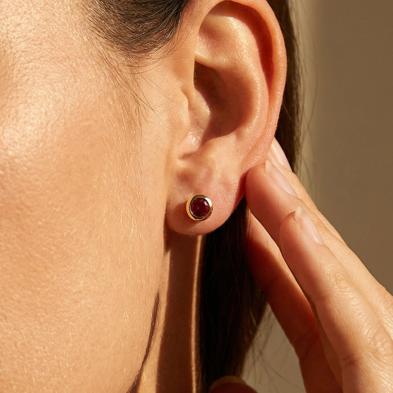 a close up of a models ear wearring a ruby yellow gold stud earring 