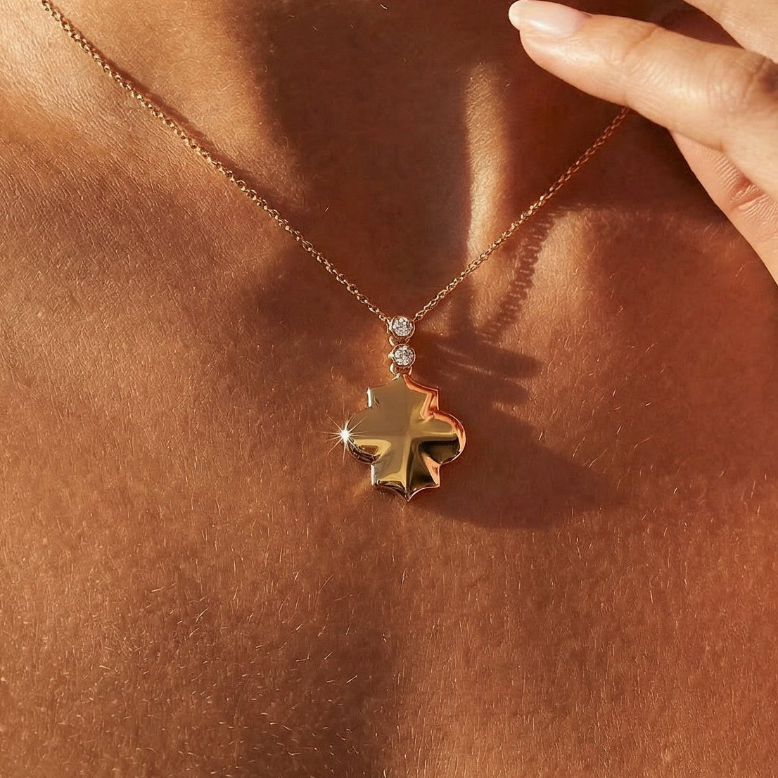 Close-up of a person wearing a gold necklace with a pendant on a neutral background